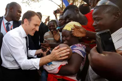 Emmanuel Macron salue une femme et son enfant, devant l'écoleLagem Taaba, à Ouagadougou.