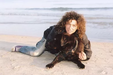 Serrant son chien contre elle, la navigatrice pose allongée dans le sable sur une plage de Marseille.