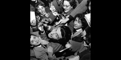 1956 - Gilbert Bécaud revient des USA. Il a retrouvé à l'Olympia outre son public habituel, 900 fidèles en uniforme: les &quot;Bécotistes&quot;. Les filles portent la robe rouge, le corsage bleu, la cravate blanche. Les garçons, le costume bleu, la chemise blanche, le gilet rouge. Leur uniforme leur donne un droit: l'entrée gratuite.Et un devoir : vouer à l'idole un culte tonitruant.Retrouvez Paris Match Vintage surFacebook,TwitteretInstagram