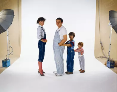 Coluche lors d'une séance photo en famille, avec son épouse Véronique et leurs fils Marius, 4 ans, et Romain, 8 ans, tous en salopette, en octobre 1980.