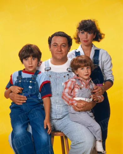 Coluche lors d'une séance photo en famille, avec son épouse Véronique et leurs fils Marius, 4 ans, et Romain, 8 ans, tous en salopette, en octobre 1980.