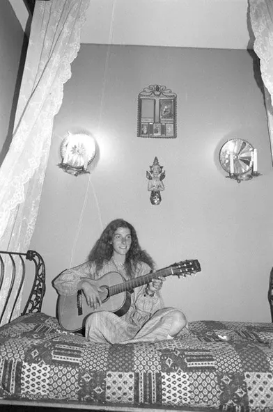 Florence Arthaud chez elle à Paris dans la grande maison familiale, jouant de la guitare assise en tailleur sur son lit à baldaquin dans sa chambre.