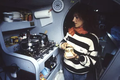 Une conserve à la main, la navigatrice est devant une cuisinière dans la cabine de son trimaran «Groupe Pierre 1er».
