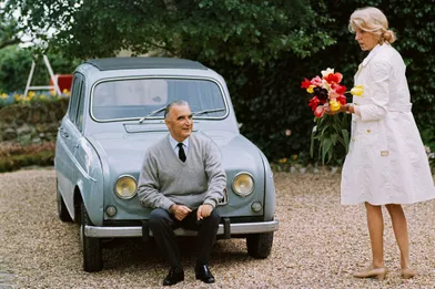 Georges Pompidou fume une cigarette assis sur le pare-chocs d'une 4L dans la cour de sa maison d'Orvilliers. A droite, sa femme Claude tient un bouquet de tulipes du jardin.