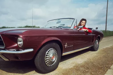 L'école est bien finie pour Sheila au volant d'une Ford Mustang cabriolet sur une route de campagne en 1967.