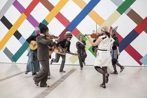 Des musiciens interprètent l’air composé par l’artiste (au centre avec plusieurs chapeaux).