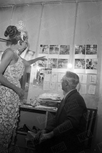 Joséphine Baker dans sa loge de l’Olympia avec « Pépère », le chiffonnier de Saint Ouen qui avait retrouvé dans une poubelle le bébé adopté par la chanteuse en décembre 1959. La chanteuse montre les photos de sa tribu «arc-en-ciel».