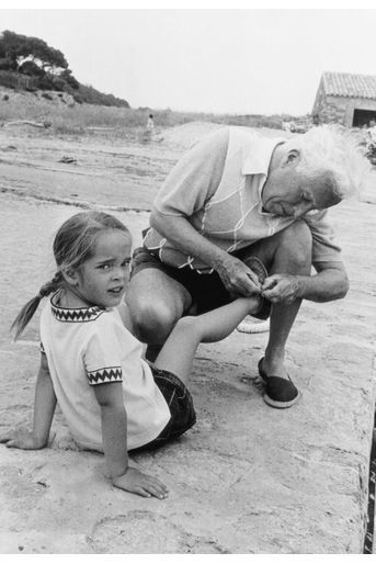 En vacances dans le Lavandou, Charlie Chaplin (1889-1977), 67 ans, aide sa fille Victoria à remettre sa sandale.