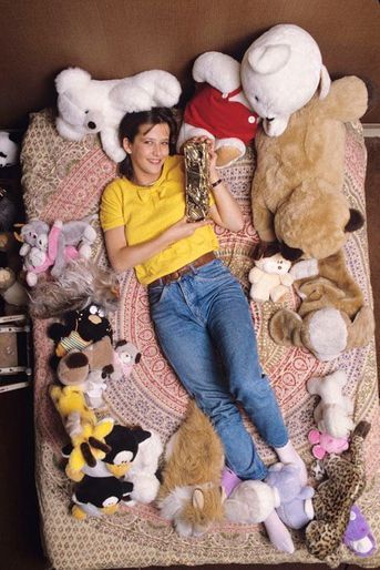 Sceaux (92), mars 1983 : Sophie Marceau, 16 ans, chez ses parents : souriante, allongée sur son lit au milieu des peluches, posant avec le César du meilleur jeune espoir féminin 1983, décerné pour le film &quot;La boum 2&quot;.