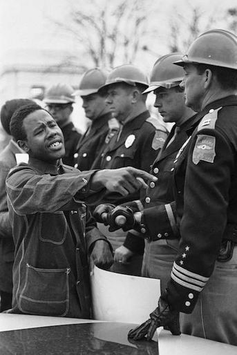 Le 19 mars 1965, un jeune homme demande aux policiers de le laisser franchir le cordon de sécurité pour participer à la marche pour les droits civiques. Par AFP. "Le travail n'est pas terminé": Barack Obama célèbre samedi à Selma (Alabama) la marche pour les droits civiques qui a marqué un tournant dans l'histoire des Etats-Unis en garantissant le droit de vote aux Afro-Américains des Etats du Sud.Le premier président noir de l'histoire des Etats-Unis doit s'exprimer devant le pont Edmund Pettus sur lequel, le 7 mars 1965, plusieurs centaines de manifestants pacifiques furent violemment repoussés par la police dans un assaut qui traumatisa l'Amérique et aboutit, quelques mois plus tard, au Voting Rights Act.Barack Obama avait trois ans au moment des faits. Il a appris cette histoire par sa mère, quand il avait "six, sept, huit ans". "Elle me donnait des tas de livres pour enfants sur la lutte pour les droits civiques. Elle mettait des chansons de Mahalia Jackson (qui fut une proche de Martin Luther King, NDLR)", a-t-il raconté à la veille de cette célébration.Le discours présidentiel intervient trois jours après la publication d'un rapport accablant du ministère de la Justice pointant les comportements discriminatoires de la police de Ferguson (Missouri), théâtre de violentes émeutes après la mort en août dernier d'un jeune Noir abattu par un policier blanc.Selma, ville de 20.000 habitants (dont 80% de Noirs), se prépare depuis plusieurs jours à ce week-end de commémoration auquel l'ancien président George W. Bush et plus d'une centaine d'élus du Congrès doivent participer.Le 15e amendement de la Constitution américaine, adopté en 1870, interdit de refuser le droit de vote à tout citoyen "sur la base de sa race ou de sa couleur". Dans plusieurs Etats du Sud, il a longtemps été bafoué."Au rythme actuel, il faudra 103 ans pour que les 15.000 Noirs du comté de Dallas puissent s"inscrire sur les listes électorales", lançait Martin Luther King en janvier 1965 à Selma.Si la loi signée le 6 août 1965 par le président Lyndon Johnson a marqué une rupture, nombre d'activistes considèrent que ce chapitre n'est pas clos.