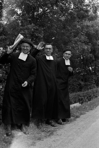 Trois prêtres sur le bas-coté de la route regardent passer le peloton.