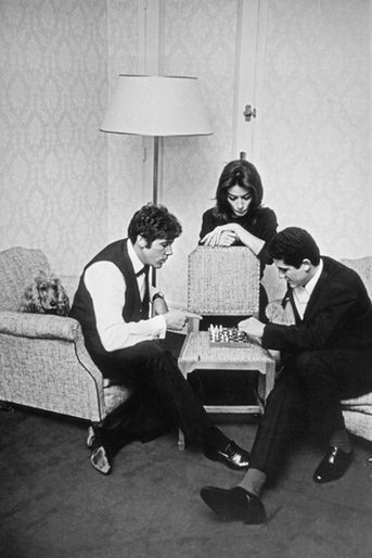 Claude Lelouch joue aux échecs avec Pierre Barouch dans une chambre d'hôtel sous le regard d'Anouk Aimée, mai 1966