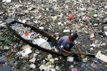 Un Indonésien sur sa barque navigue au milieu de déchets.