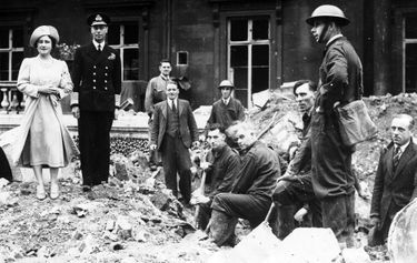 Précédant son mari, George VI, en uniforme, Elisabeth enjambe hardiment les décombres devant le palais de Buckingham, après le bombardement du 10 septembre 1940.