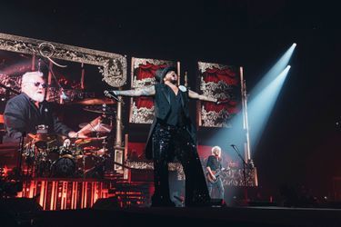 Adam Lambert peut commencer son numéro de charme : vêtu d’un chapeau haut de forme, bras tatouée et voix impeccable. Derrière lui et sur l'écran, le batteur métronome Roger Taylor.