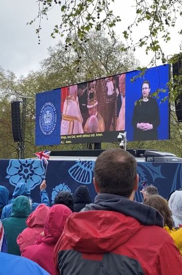 Devant l'écran de St James's Park, sous la pluie, on applaudit et on ouvre des bouteilles de pétillant au moment de voir la couronne de Saint Edouard se poser sur la tête de Charles III. Le 6 mai 2023 à Londres.