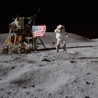 L'astronaute John W. Young, commandant de la mission Apollo 16, saute depuis la surface lunaire, devant le drapeau américain.