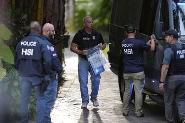 A law enforcement agent carries a bag of evidence to a van as federal agents stand at the entrance to a property belonging to rapper Sean 