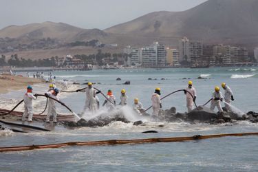 Décapage à haute pression des rochers de la plage Los Pocitos dans le golfe d’Ancon, au nord de Lima, le 11 février. Devant, un boudin flottant qui retient les hydrocarbures.