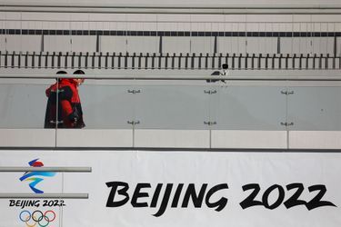 Des membres du personnel passent devant un panneau Pékin 2022 au Centre national de saut à ski lors d'une tournée médiatique organisée par le gouvernement sur les sites des Jeux olympiques d'hiver de Pékin 2022 à Zhangjiakou.