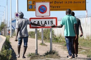Des migrants devant le panneau marquant l'entrée de Calais.