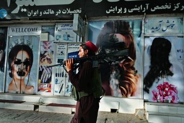 Un taliban armé d&#039;un M16A2 américain, devant les affiches défigurées d&#039;un salon de beauté de Shahr-e Naw, un quartier du nord-ouest de la capitale.
