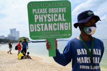 Une personne tient une pancarte rappelant aux gens d&#039;observer la distanciation physique lorsqu&#039;ils visitent la partie récemment rouverte de la baie de Manille remplie de sable blanc artificiel. 