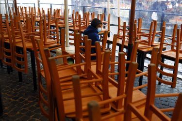Un homme assis entre les chaises d'un restaurant fermé en Italie. 