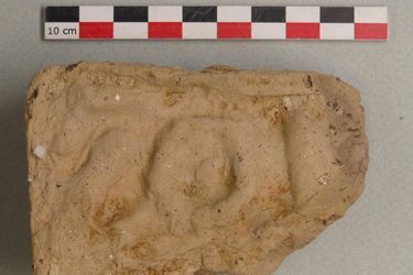 Fragment d’antéfixe (ornement de toiture) en terre cuite de fabrication massaliète. Il porte un décor moulé non identifiable.
