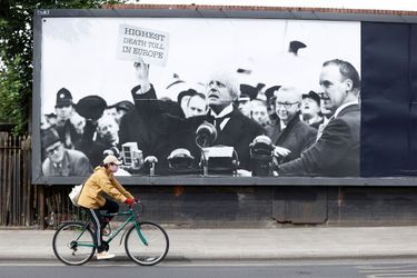 Un personne portant un masque passe en vélo devant une affiche montrant le Premier ministre britannique brandissant un feuille sur laquelle il est écrit: "Plus forte mortalité d'Europe". 