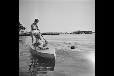 Le 8ème Festival de CANNES se déroule du 26 avril au 10 mai 1955 : attitude riante de Brigitte BARDOT (20 ans) et Brigitte FOSSEY (8 ans et demi) sur une sorte de barque, BB debout une rame à la main tandis que son chien cocker, &quot;Clown&quot; revient vers elles à la nage, un baton dans la gueule.