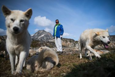 A Kulusuk, un village insulaire du Groenland, un chasseur pose avec son chien, devant un paysage sans glace.