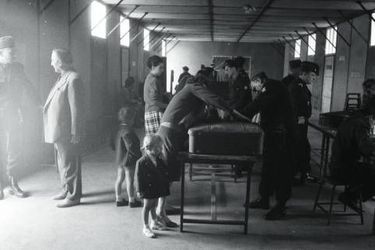 Le 12 mai 1962. Des rapatriés d’Algérie en partance de Constantine. Dans un hangar, des familles françaises passent devant des policiers pour enregistrement et contrôle des valises avant d’embarquer dans des bus à destination de Marseille. 