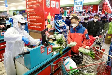Un caissier dans une combinaison de protection sert des clients dans un supermarché à Wuhan, le 12 février 2020