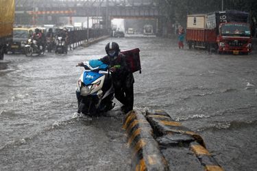 Un coursier pousse son scooter dans une route inondée de Mumbai en Inde le 5 août 2020