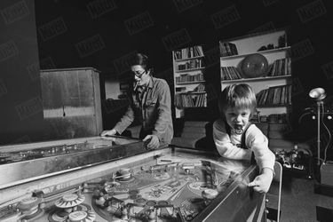 Jacques Dutronc et son fils Thomas (2 ans et demi) jouent au flipper, dans leur maison du XIVème arrondissement de Paris, en janvier 1976.