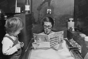 Jacques Dutronc prend son bain, cigare aux lèvres et Lucky Luke dans les mains, sous le regard de son fils Thomas (2 ans et demi), dans leur maison du XIVème arrondissement de Paris, en janvier 1976.