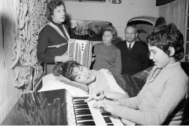Rika Zaraï chez elle, allongée dans son lit dans un corset de plâtre, après son accident de voiture, entourée de ses parents Madame et Monsieur Goussman, son accordéonniste Marceau Magnier et sa fille Yael à l&#039;orgue, en janvier 1970.