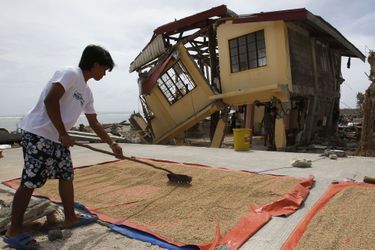 Dans la province de Samar, la vie continue malgré tout pour cet homme qui sèche le son de riz, devant sa maison fendue en deux par le typhon.
