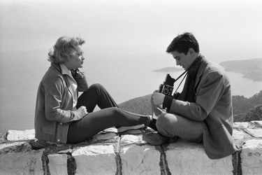 Un mois après leurs fiançailles officielles, Romy SCHNEIDER et Alain DELON passent Pâques sur la Côte d'Azur : Alain 24 ans assis en tailleur sur un muret dominant la mer photographiant Romy assise en face de lui.