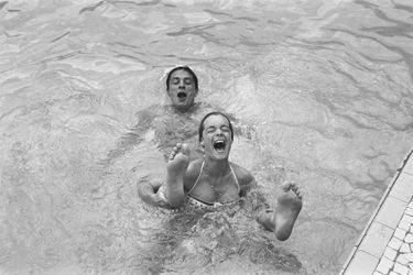 Romy SCHNEIDER riante, bouche grande ouverte, tenant les jambes d&#039;Alain DELON alors qu&#039;ils se baignent dans la piscine du Beach à MONACO.