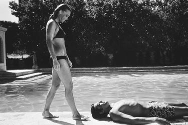Tournage du film "La piscine" de Jacques DERAY dans le décor d'une somptueuse villa aux environs de Saint-Tropez pourvue d'une immense piscine : Romy SCHNEIDER de profil s'approchant d'Alain DELON allongé au bord de la piscine, tous deux en maillot de bain.