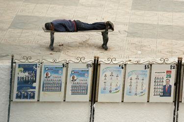 Un homme dort sur un banc à proximité des affiches de campagne pour les élections législatives, à Alger, le 25 avril 2017. 