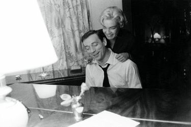 Simone Signoret auprès de son mari Yves Montand qui joue du piano, chez eux à Paris, après le retour de l'actrice d'un tournage.