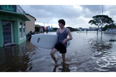 Un habitant de Brisbane marche dans la ville, planche de surf à la main. Les inondations en Australie ont causé 14 morts dans le pays depuis lundi.