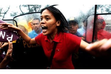  Une jeune Philippine manifeste, dos aux policiers anti-émeutes, dans les rues de Manille. Elle proteste pour le maintien de la journée de la femme, demain, et contre les politiques du gouvernement actuel.