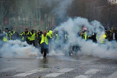 Des «gilets jaunes» dégagent des grenades lacrymogènes sur les Champs-Elysées, samedi.