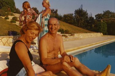 Louis DE FUNES et son épouse Jeanne, tous deux souriants, en maillot de bain assis au bord d&#039;une piscine, en vacances.