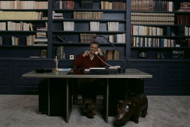  En France, à Paris, en février 1987, Roger HANIN, acteur, chez lui, assis sur son bureau, devant sa bibliothèque.