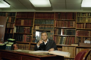 En France, à Paris, le 22 janvier 1990, Roger HANIN, acteur, assis à un bureau, lisant, dans sa bibliothèque, chez lui.